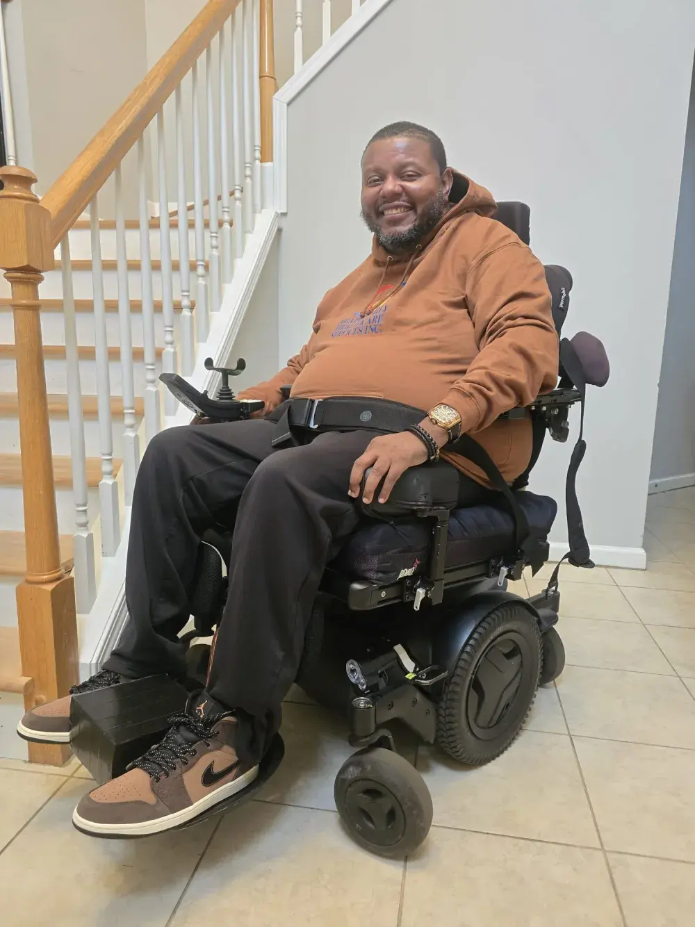 Lamont McLeod smiling in his power wheelchair at the foot of a staircase